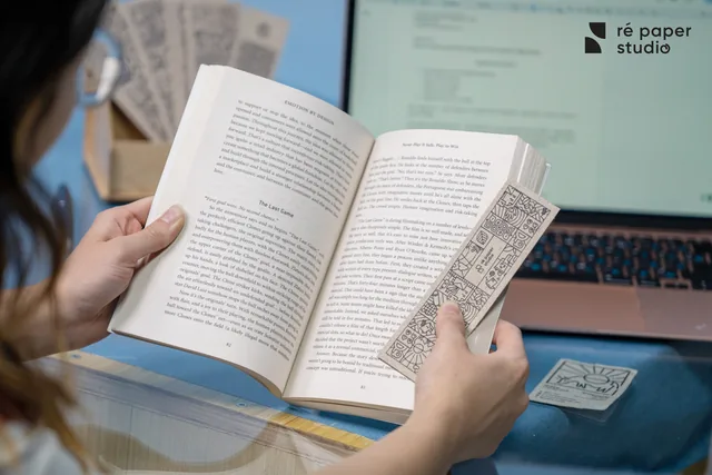 A reader holding a line-art bookmark inside an open book