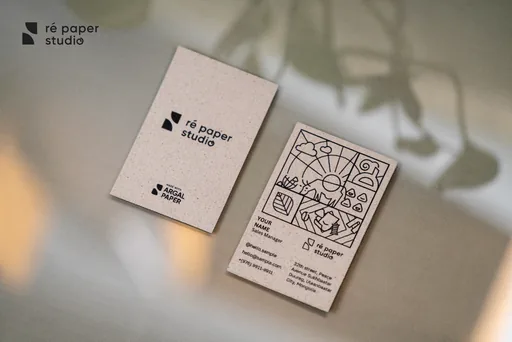 Two Ré Paper business cards on argal paper — logo on the front, line-art illustration on the back